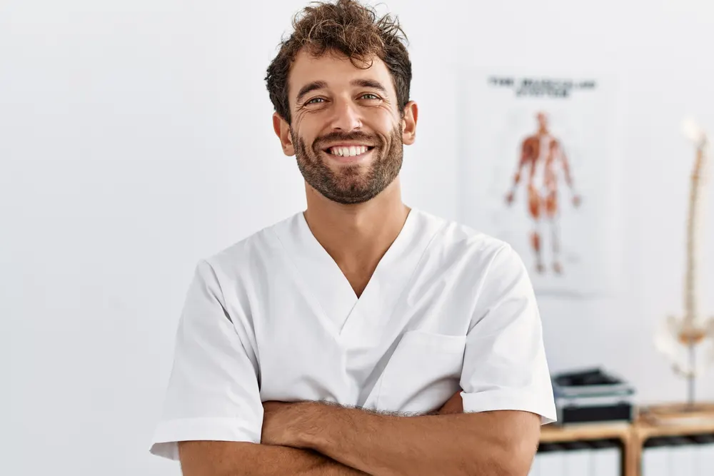 Chiropracteur souriant, bras croisés, dans son cabinet